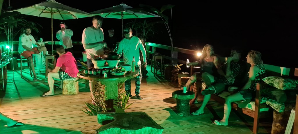 Happy hour de um grupo de homens e mulheres no deck da pousada Sucunduri com iluminação esverdeada