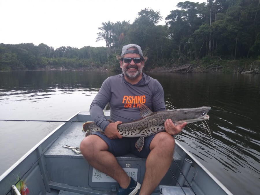 Amigo Taveira sentado no barco mostrando um caparari que ele pescou